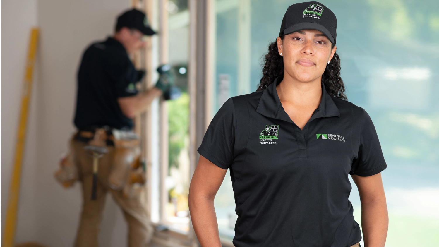 Renewal by andersen female installer standing infront of a window, while there is another installer in the background tightening the windows