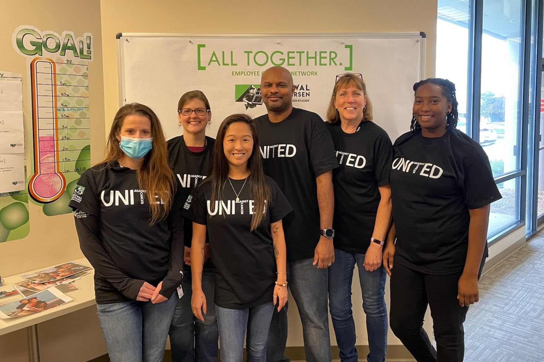 Group of RbA employees in United Against Cancer T-shirts in front of fundraising thermometer.