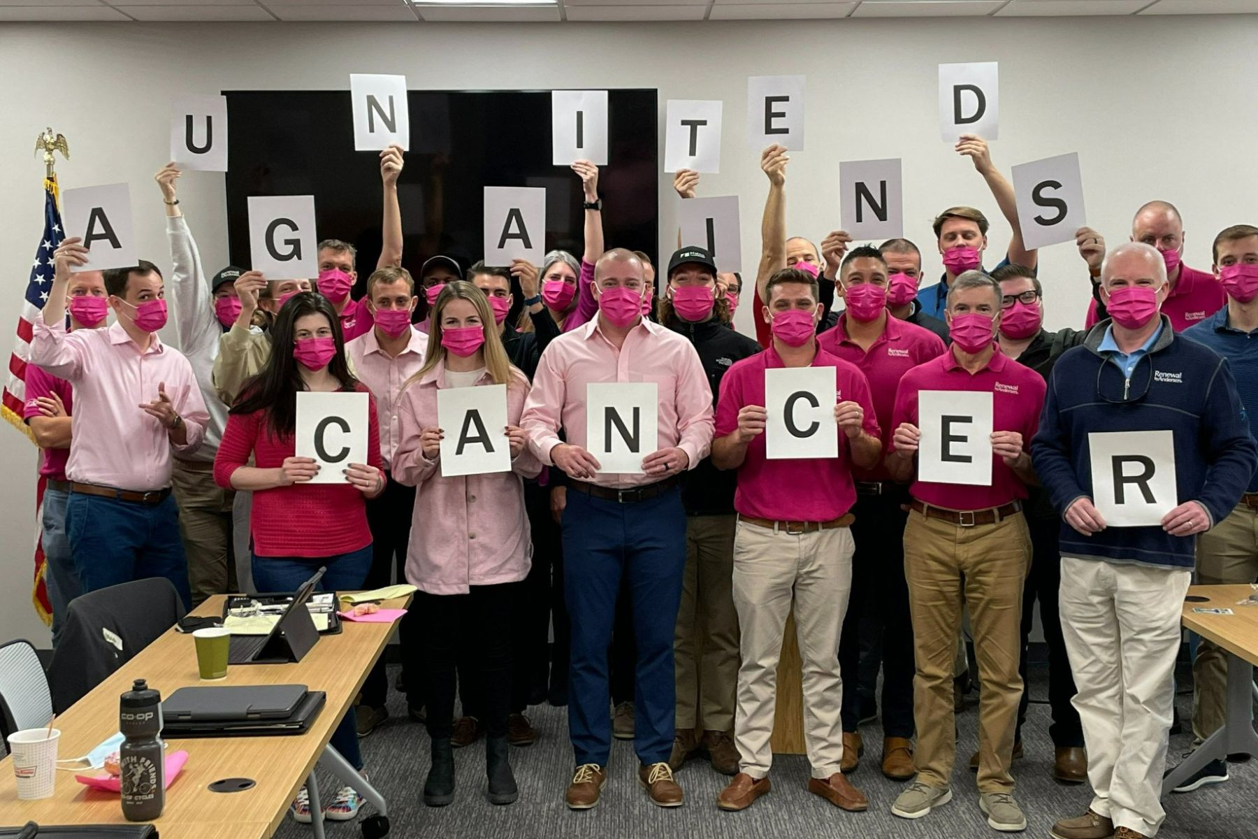 Group of RbA employees in pink masks holding letters that spell out "United Against Cancer". 