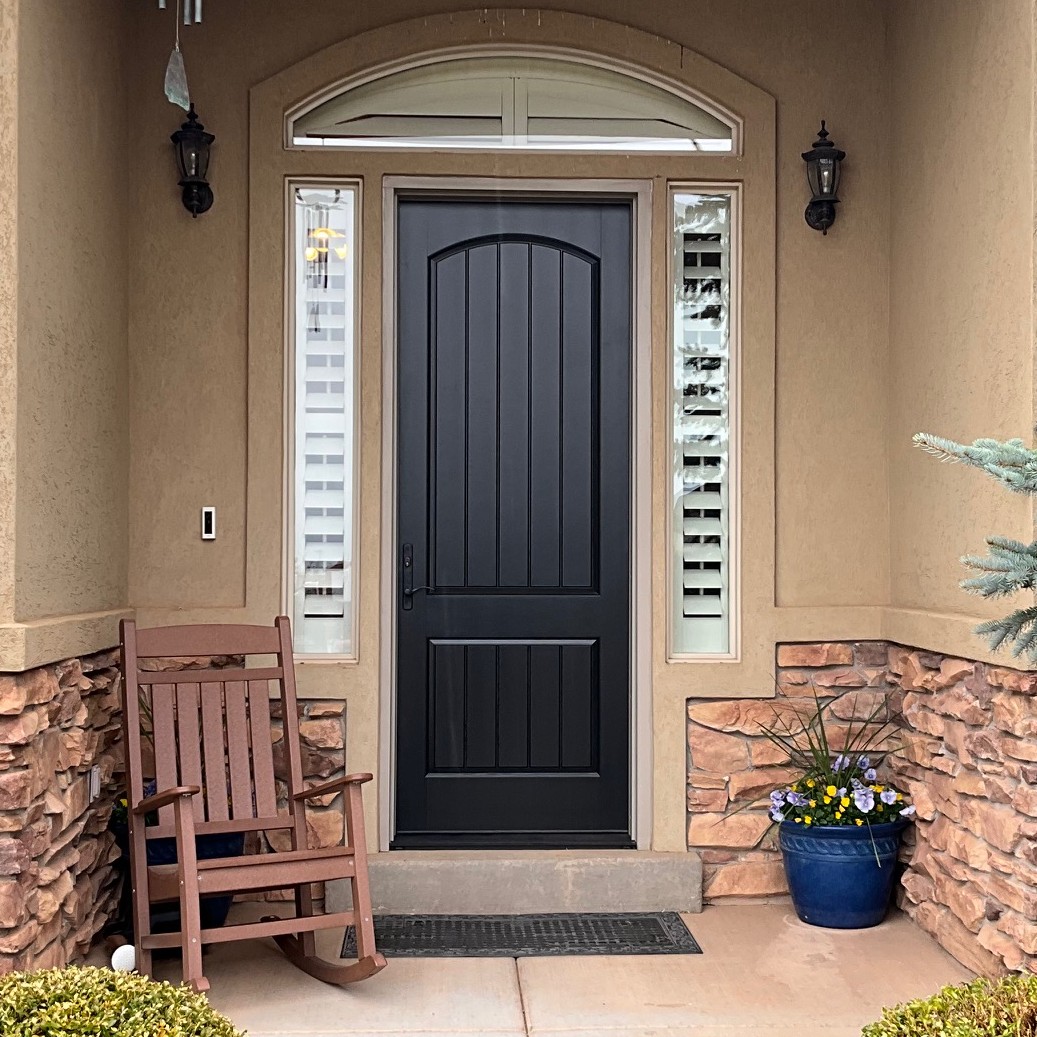 A single panel Ensemble entry door. The door is solid black. There is a rocking chair in the picture.