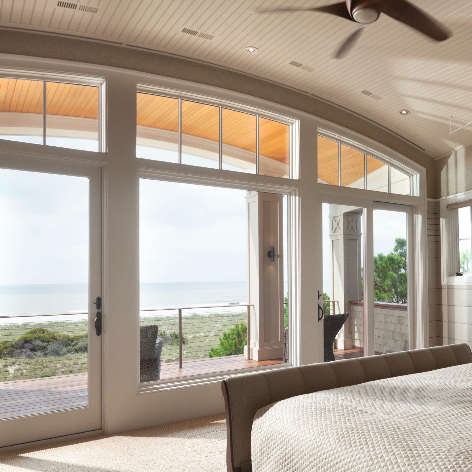 A window wall of sliding glass doors in white. The doors have a full-length transom that is custom on top. It is an arched transom.
