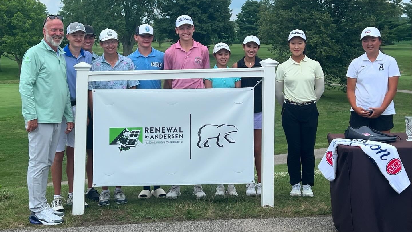 Group of individual stand on a golf course behind a Renewal by Andersen sign.